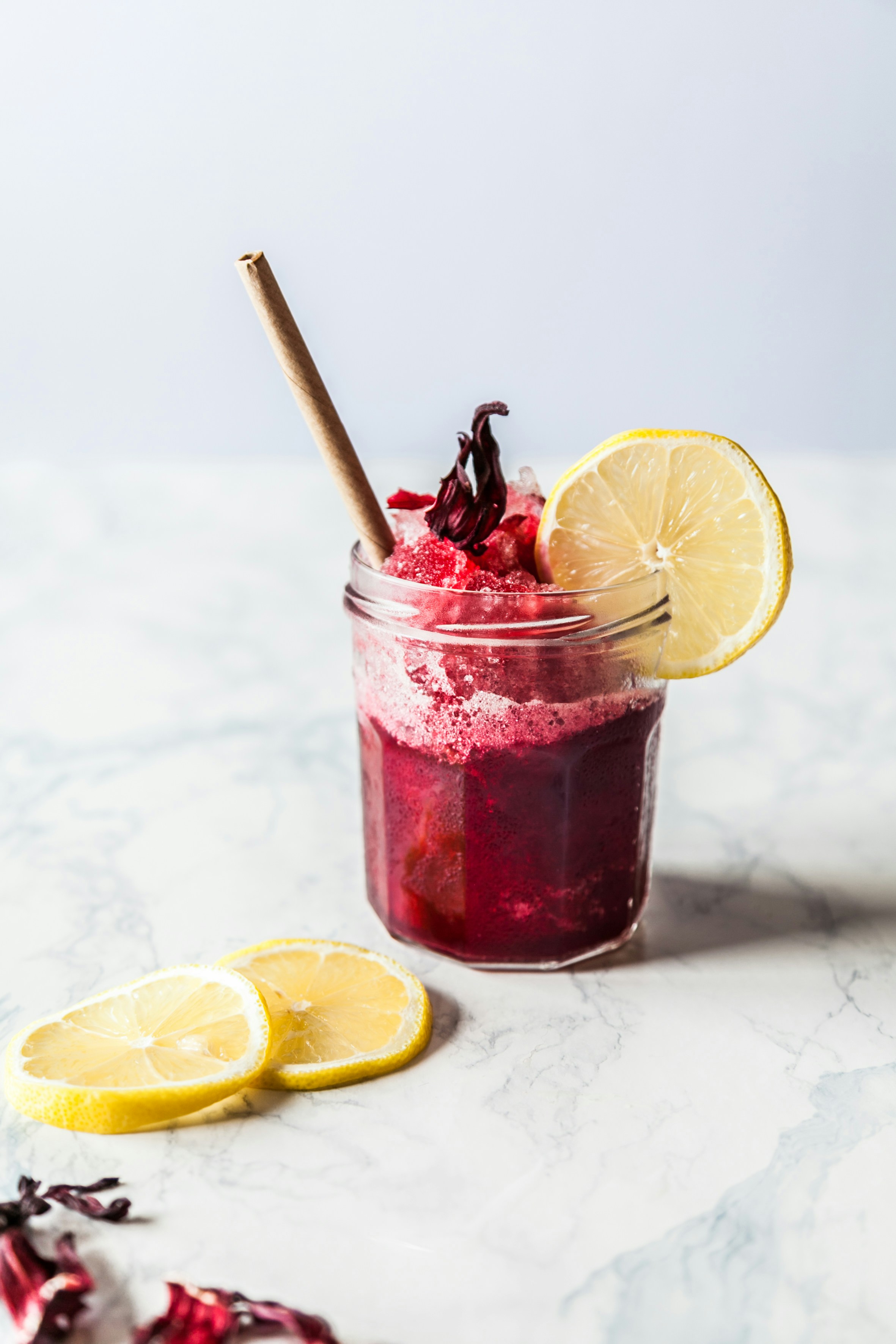 Exemple d&#39;image de base. Un bocal en verre contient un liquide rouge avec une tranche de citron sur le côté et une paille qui dépasse. Des tranches de citron sont visibles au premier plan à gauche.